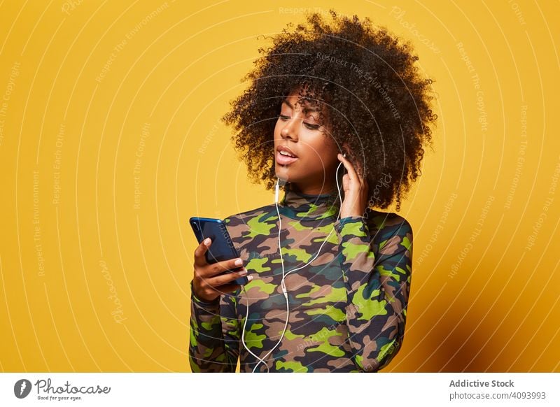 Trendige junge Frau mit Smartphone beim Musikhören trendy Farbe Kopfhörer zuhören Mode Afro-Look Afroamerikaner schwarz ethnisch Stil Spaß Klang lässig
