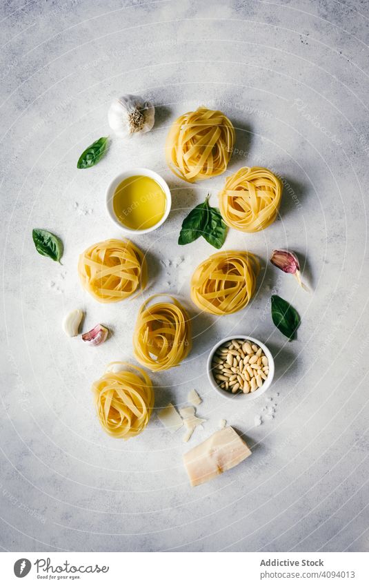 Nester von Tagliatelle-Nudeln mit Basilikumblättern und Knoblauch auf dem Tisch Spätzle Pesto angeordnet roh Pinienkerne Küchenkräuter weiß Bestandteil Käse