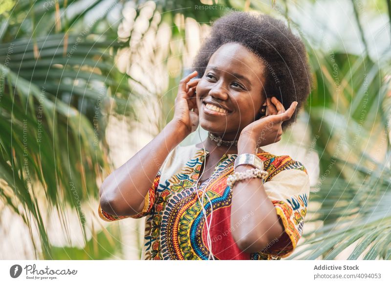 Lächelnde schwarze Frau beim Hören von Musik zuhören Kopfhörer Afrikanisch Handfläche traditionell farbenfroh Freude ethnisch heiter Glück Melodie Audio Gesang