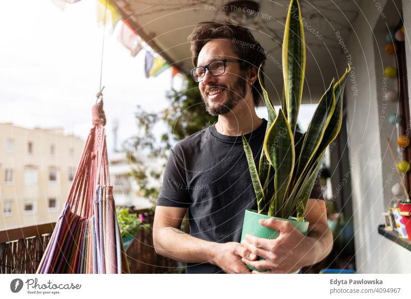Junger Mann, der sich um seine Pflanzen auf einem Balkon kümmert Hängematte Sansevieria Topfpflanze Sperrung zu Hause bleiben Pflege gutaussehend Hipster urban