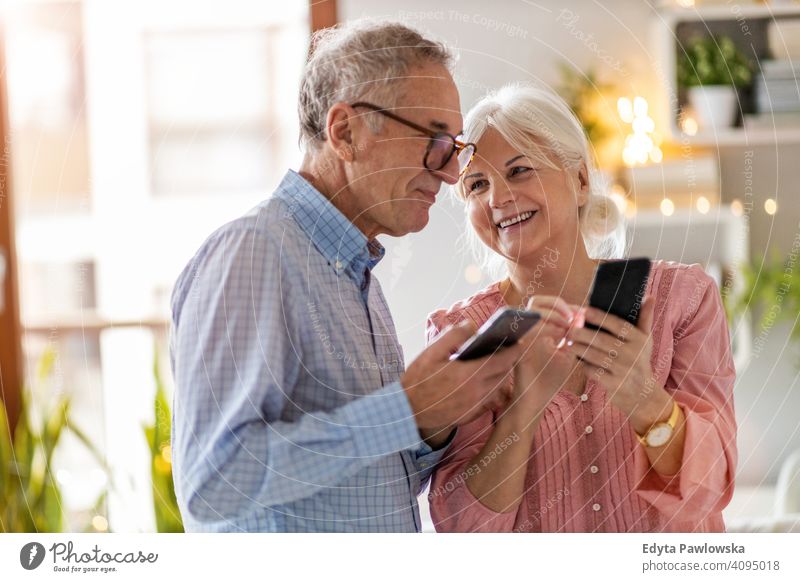 Älteres Ehepaar benutzt Mobiltelefone zu Hause Menschen Frau Erwachsener Senior reif lässig attraktiv männlich Mann Lächeln Glück Kaukasier zahnfarben genießend