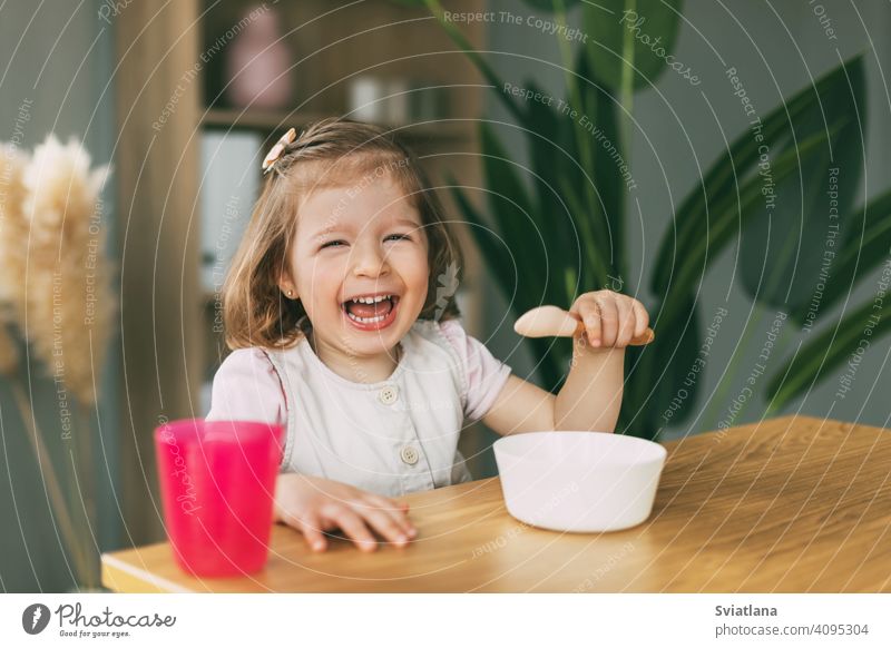 Ein kleines Mädchen isst Brei aus einer weißen Schüssel, ein Mädchen frühstückt am Tisch sitzend. Gesundes Frühstück, gesundes Essen Gesundheit Kind Haferbrei