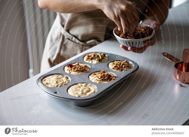 Gesichtslose Person beim Backen von Muffins mit Walnüssen Bäcker Walnussholz Essen zubereiten Nut bestäuben selbstgemacht Vorbereitung Teigwaren Cupcake