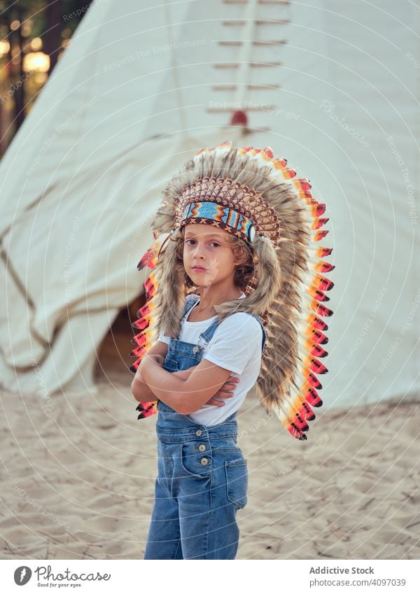 Zufriedenes Kind mit authentischem Hut im Zelt Junge Wigwam Inder Feder Inhalt erfreut Latzhose Jeansstoff Stehen verschränkte Arme Portugal Park Freizeit