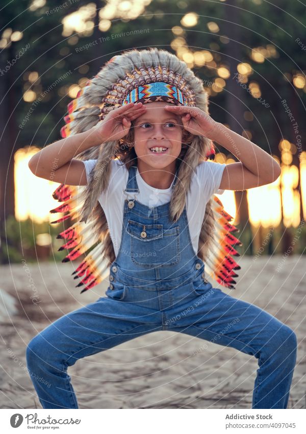 Zufriedenes Kind mit authentischem Hut im Zelt Junge Wigwam Inder Feder Inhalt erfreut Latzhose Jeansstoff Stehen verschränkte Arme Portugal Park Freizeit