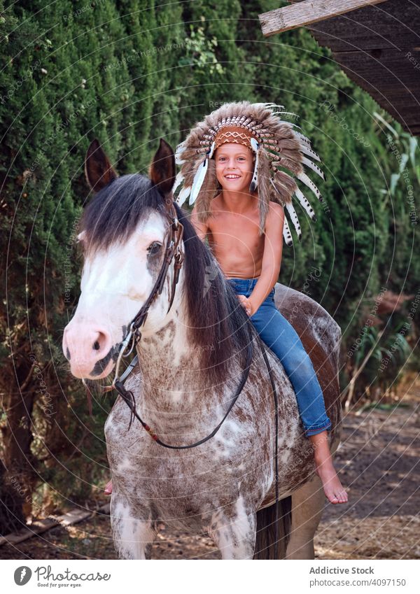 Glückliches Kind sattelt Hengst Junge Pferd Mitfahrgelegenheit authentisch Sattel Kriegsmütze Inder Tracht Training heimatlich Kunst Kopfschmuck Kopfbedeckung