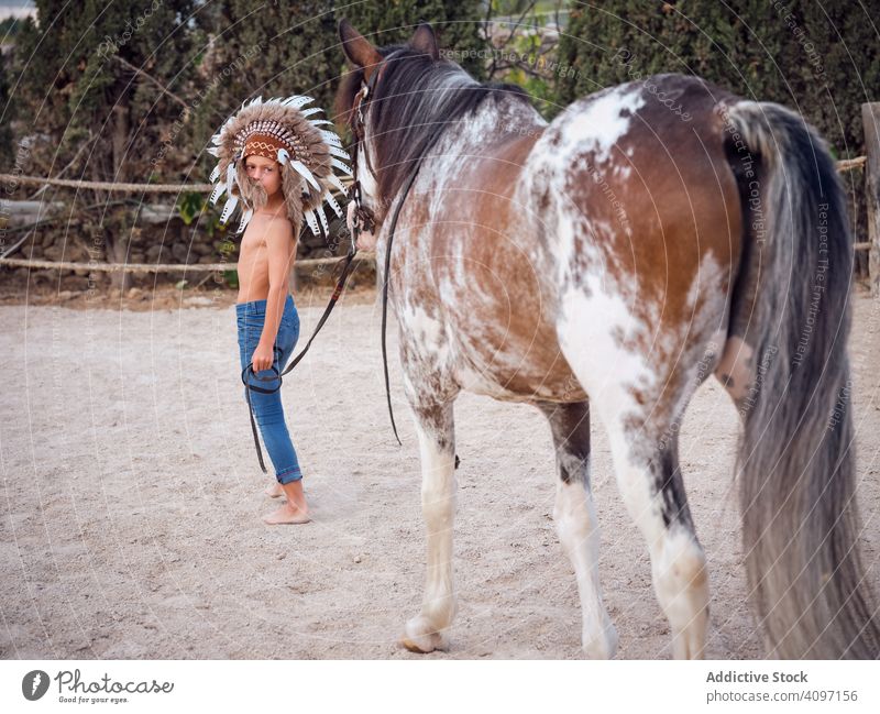 Ruhiger Junge hält Geschirr und geht mit Hengst Pferd Bauernhof Windstille ruhig Cowboy Harmonie Feder Kriegsmütze authentisch Inder Liebe Art Sand ohne Hemd