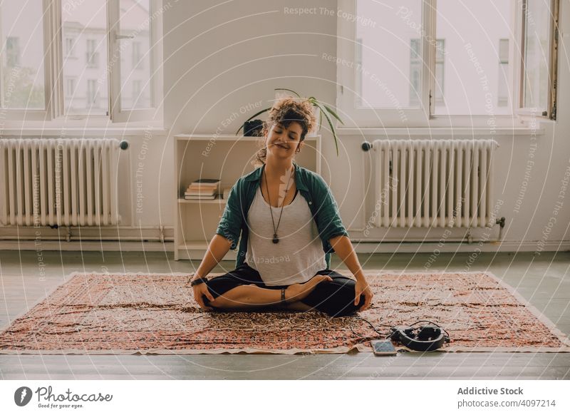 Friedliche Frau meditiert im Lotussitz auf dem Boden zu Hause meditierend friedlich entspannt Lächeln lässig sitzen Stock Teppich heimwärts Appartement modern