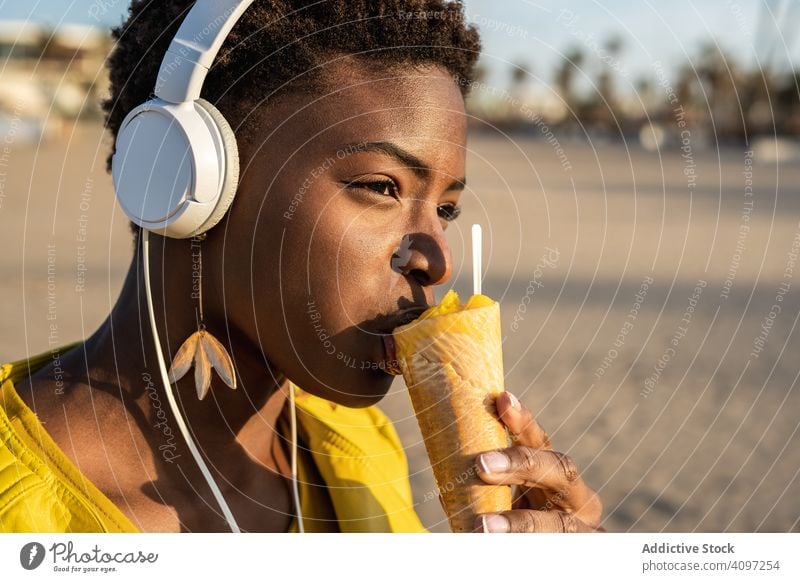 Kühle Frau isst Eiscreme am Strand Speiseeis trendy cool essen wüst Afroamerikaner Jacke gelb hell Sonnenbrille genießen süß Lebensmittel Sommer Spaß Sahne