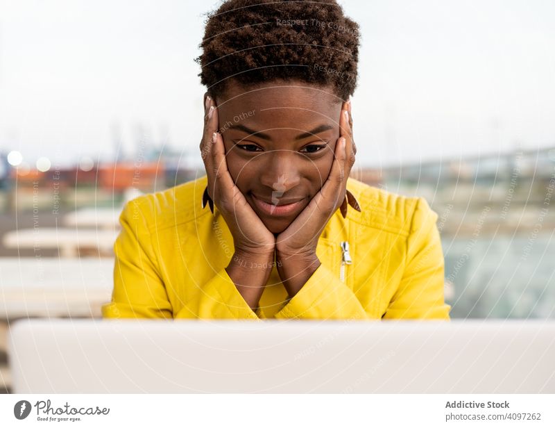 Frau arbeitet am Laptop am Tisch benutzend Arbeit Schreibtisch Großstadt Afroamerikaner Jacke gelb hölzern jung lässig Arbeitsplatz beschäftigt abgelegen