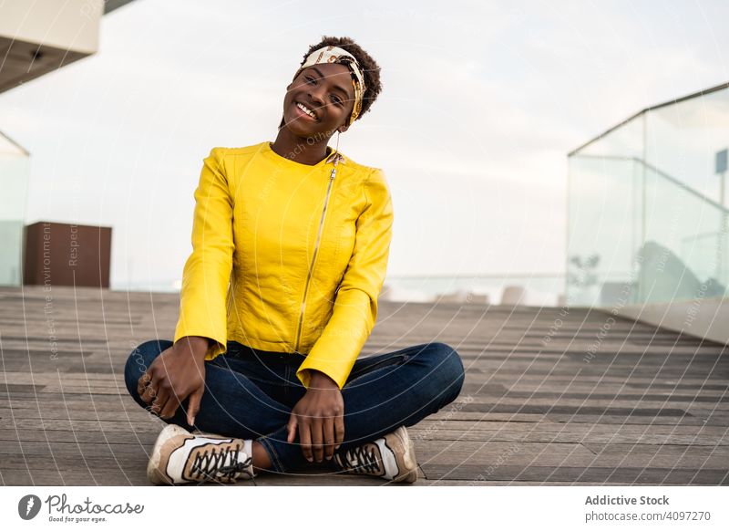 Intelligente Frau sitzt auf einem hölzernen Fußweg stylisch Kälte sich[Akk] entspannen modern klug Stock Jacke Afroamerikaner jung cool trendy Glück Zeitgenosse