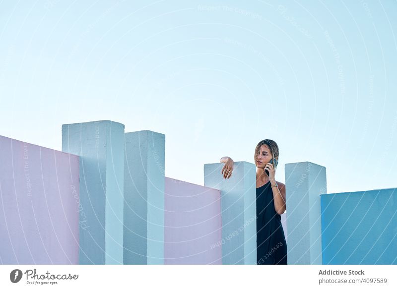 Frau steht auf dem Dach eines blauen Gebäudes und benutzt ein Mobiltelefon lässig elegant Konstruktion Struktur geometrisch Architektur urban Fassade Wand
