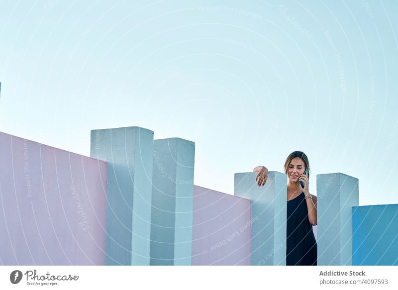 Frau steht auf dem Dach eines blauen Gebäudes und benutzt ein Mobiltelefon lässig elegant Konstruktion Struktur geometrisch Architektur urban Fassade Wand