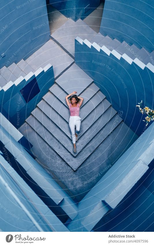 Frau liegend auf modernem blauen Gebäude lässig Lügen Stock Treppe im unteren Stockwerk elegant Konstruktion Struktur geometrisch Architektur urban Fassade