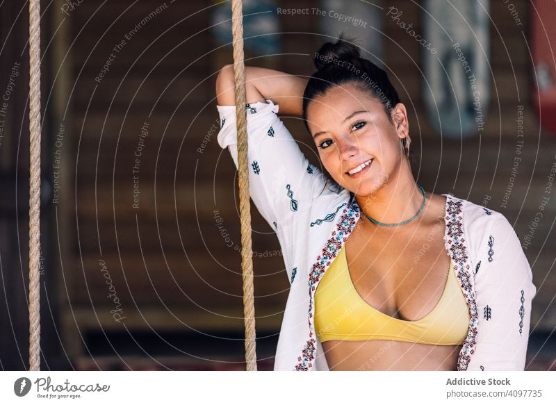 Fröhliche Frau beim Schaukeln auf einer tropischen Terrasse Mitfahrgelegenheit heiter Lächeln Bräune Glück lässig sitzen ruhen Holzwand Costa Rica jung
