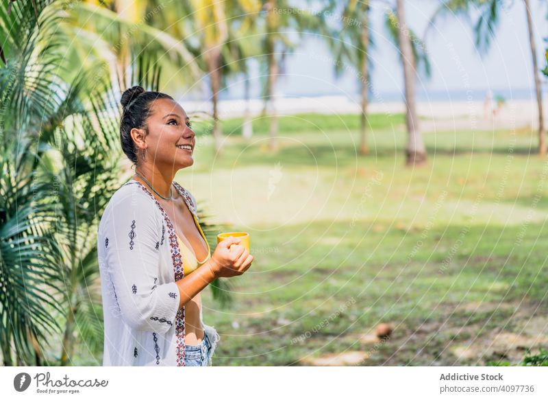 Entspannte Frau genießt heißes Getränk und steht auf exotischem Rasen entspannt Heißgetränk Seeküste Palme sonnig trinken friedlich Kaffee Becher stehen Gras