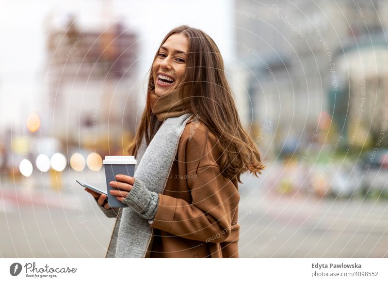 Lächelnde junge Frau mit Smartphone und Kaffeetasse im Freien in städtischer Umgebung Herbst fallen Mädchen schön Wetter Mantel Mode hübsch attraktiv