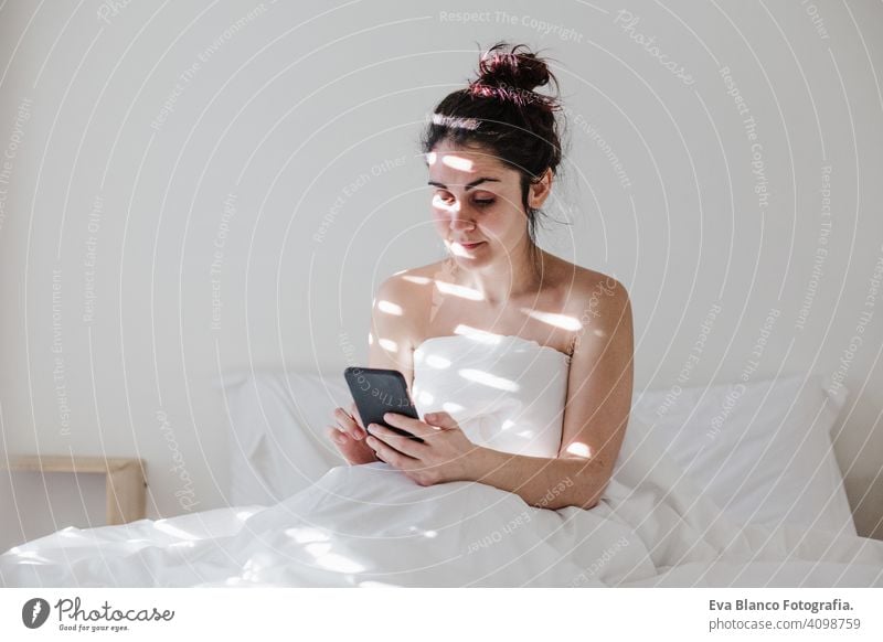 attraktive junge kaukasische Frau entspannt gut im Bett während der Morgenzeit. Dame mit Mobiltelefon im Schlafzimmer Handy Technik & Technologie Kaukasier