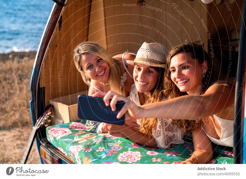 Entspannt Mädchen Freunde nehmen selfie bequem Platzierung auf Kofferraum des blauen Auto Frauen Selfie nehmen Smartphone PKW umarmend benutzend reisen Minivan