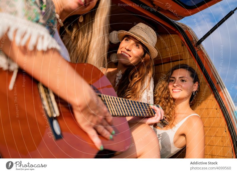 Fröhliche Frauen mit Musikinstrument, die sich während einer Autoreise im Auto ausruhen reisen Freund Gitarre Gesang Glück Kleintransporter spielen Reise