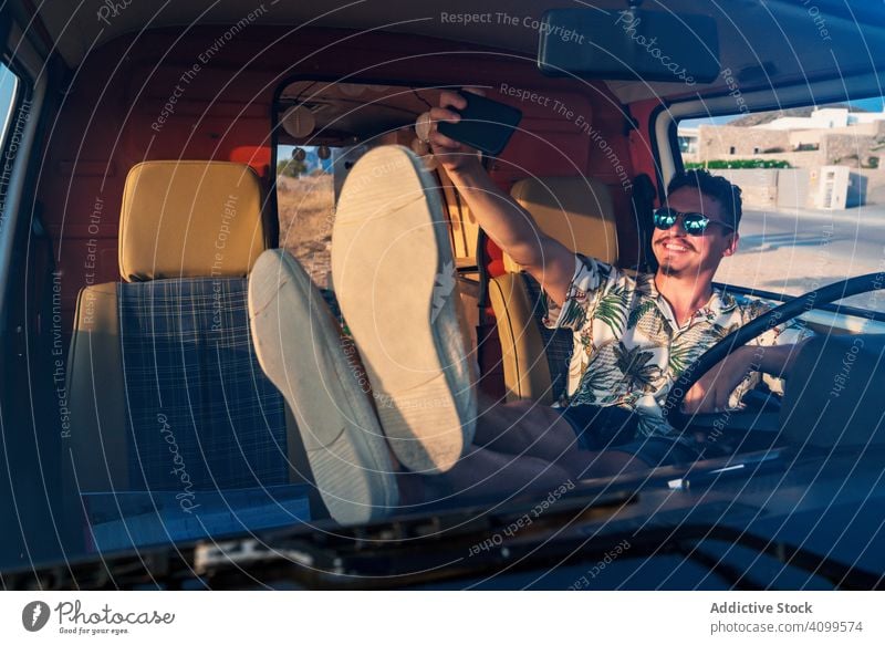 Glücklicher erwachsener Mann, der sich mit einem Smartphone selbstständig macht, während er im Lieferwagen sitzt Selfie Kleintransporter reisen Autoreise heiter