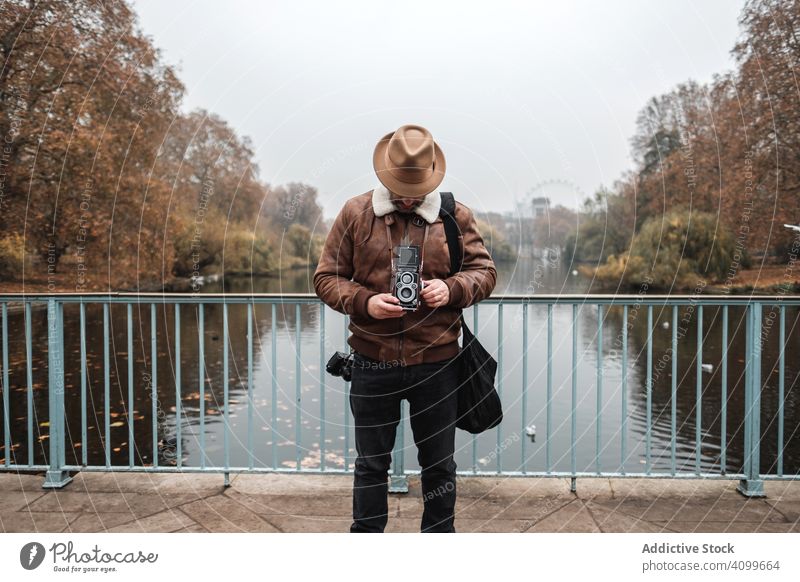 Männlicher Tourist mit altertümlicher Kamera am Fluss Fotoapparat Park Brücke Mann Herbst Windstille London Großbritannien reisen Wasser retro altehrwürdig