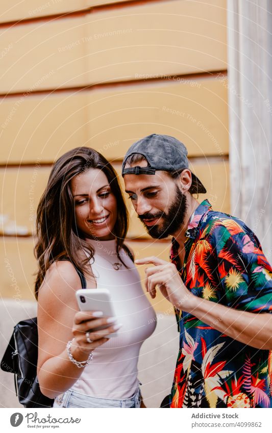 Trendiger ethnischer Mann und Frau, die sich ein Handy teilen, um Fotos zu überprüfen, während sie auf der Straße stehen Freund Telefon urban schlendern trendy