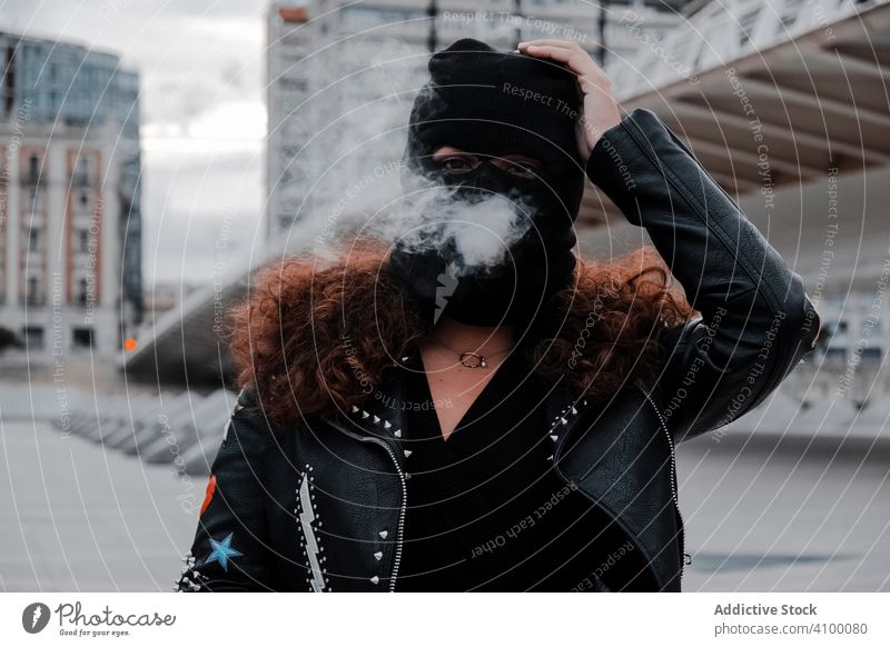 Frau in schwarzer Maske und Jacke raucht auf der Straße Rauchen Sturmhaube Mundschutz Leder Felsen urban Stil streifen brünett Mode Großstadt Outfit jung