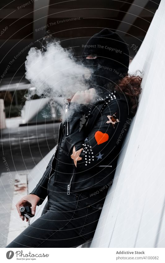 Frau in schwarzer Maske und Jacke raucht auf der Straße Rauchen Sturmhaube Mundschutz Leder Felsen urban Stil streifen brünett Mode Großstadt Outfit jung