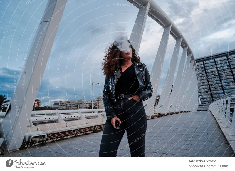 Stilvolle Frau in schwarzer Jacke und Jeans rauchend auf Brücke Rauchen urban Leder Felsen Großstadt streifen Straße brünett Mode Outfit jung unterirdisch