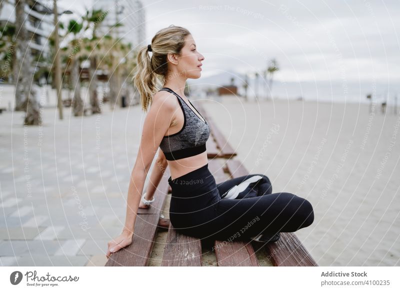 Sportlerin ruht sich auf einer Bank am Sandstrand aus Frau strecken trainiert. Arme Hände Sitzen durchkreuzen Beine Fitness Gesundheit Training Athlet