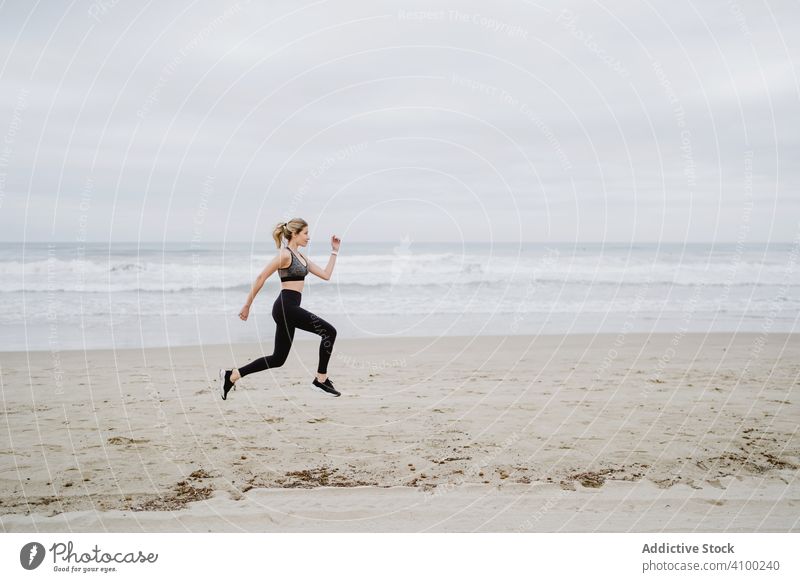 Junge Sportlerin in aktiver Kleidung beim Joggen und Springen am Meeresstrand Frau Strand springend Sommer Gesundheit Läufer Training Übung Aktivität Lifestyle