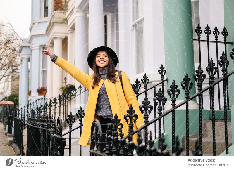 Gut gelaunte Frau, die auf der Straße ein Taxi ruft fangen Kabine winkende Hand Haus Lächeln stylisch London vereinigtes königreich Großstadt Stadt Mantel Hut