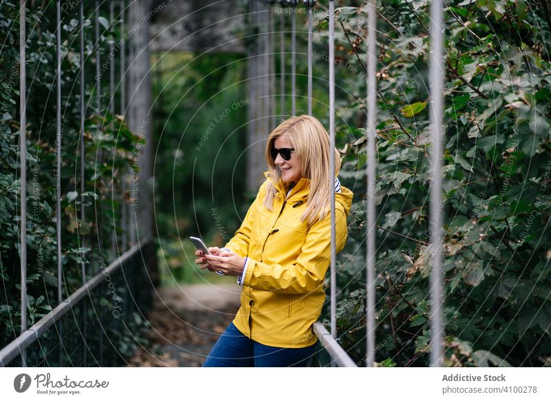 Glückliche weibliche Reisende nehmen Selfie auf Hängebrücke im Sommer Reisender Steg Smartphone Frau Wald Suspension Brücke Selfie nehmen Funktelefon erhängen