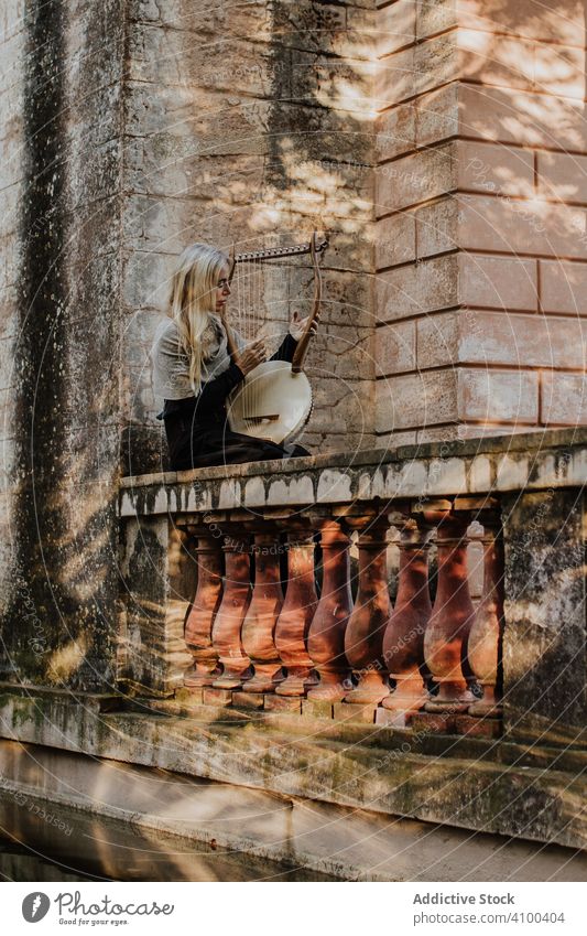 Konzentrierte Frau spielt Leier auf einer alten Terrasse Romantik Instrument lyra Ballade Musical Stein spielen Gebäude talentiert historisch sonnig Kunst