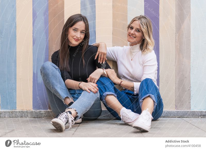 Glückliche Freundinnen sitzen vor einer bemalten Stadtmauer urban Wand Zusammensein Frauen Freundschaft berühren trendy heiter positiv stylisch Partnerschaft