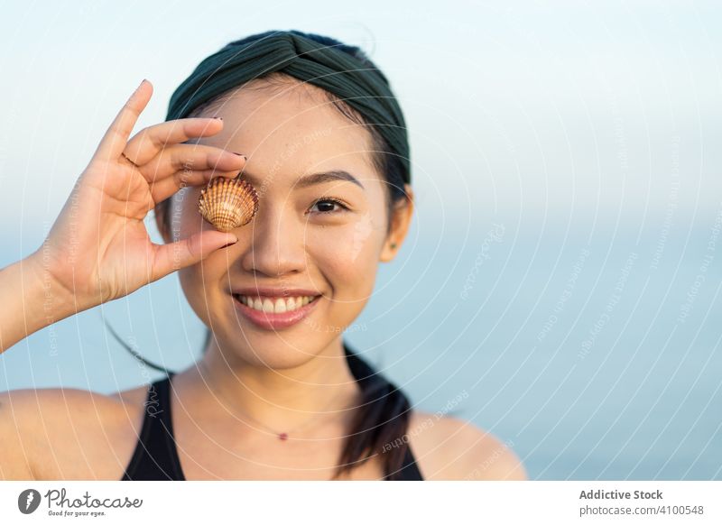 Glückliche asiatische Frau bedeckt Auge mit Muschel sportlich Strand passen Lächeln heiter freudig aktiv ethnisch MEER Sommer genießen Gesundheit Sportlerin