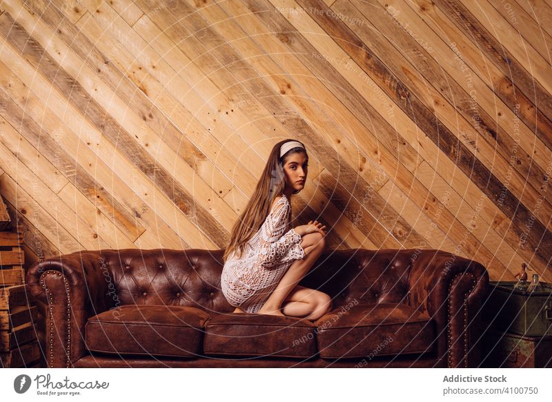 Junge Frau in weißem Kleid sitzt auf einer Couch jung Sitzen Liege Innenbereich Hipster braun Beine Mode Porträt Person hölzern Raum Menschen Mädchen Sofa Holz