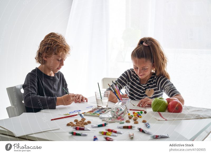 Fokussierte Kinder malen am Tisch Farbe Wasserfarbe Pinselblume fokussiert Freund heimwärts Kunst kreativ Bildung sitzen Zusammensein Mädchen Junge Pigment