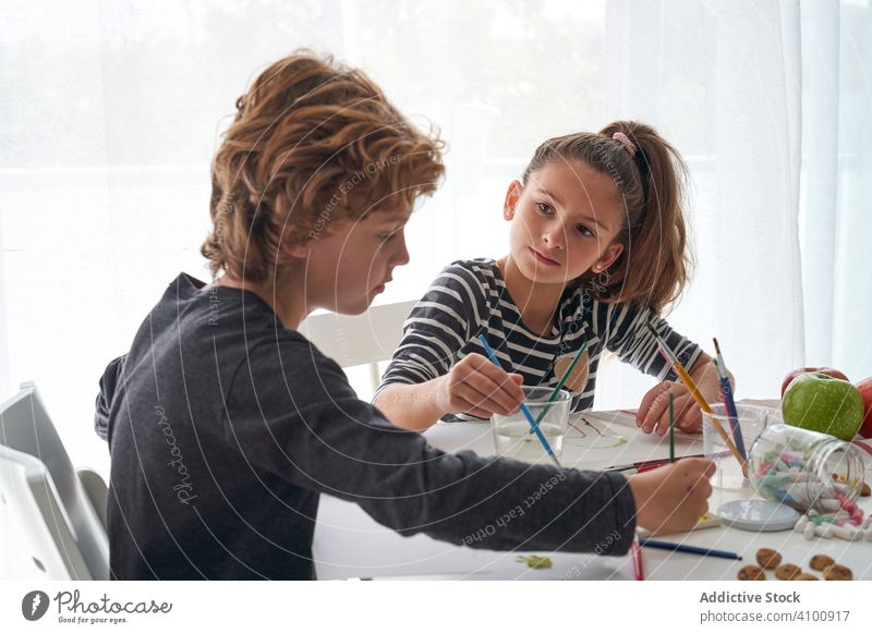 Fokussierte Kinder malen am Tisch Farbe Wasserfarbe Pinselblume fokussiert Freund heimwärts Kunst kreativ Bildung sitzen Zusammensein Mädchen Junge Pigment