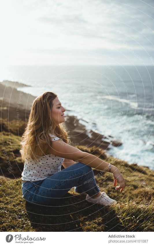 Nachdenkliche Frau im Gras sitzend mit Blick aufs Meer verträumt Küste besinnlich Horizont Sitzen Freiheit Inspiration Harmonie Seeküste bewölkter Himmel Stil