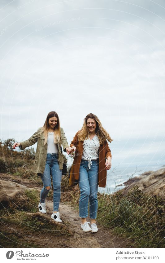 Glückliche Freundinnen, die am Meer spazieren gehen Frauen Spaziergang Nachlauf Seeküste Hügel Schwester Berge u. Gebirge Landschaft Zusammensein abstützen