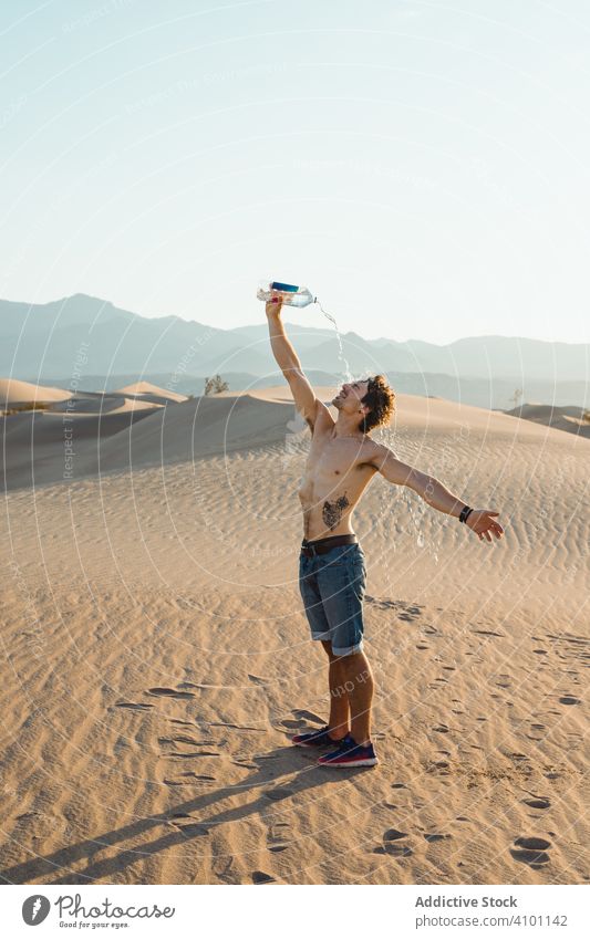 Durstiger Mann mit nacktem Oberkörper trinkt Wasser und streckt die Hände in der Wüste aus trinken wüst Dunes reisen durstig nackter Torso Gießen strecken