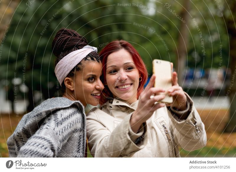 Fröhliche multirassische Freundinnen machen ein Selfie mit ihrem Smartphone im Park Paar Lächeln Partnerschaft Zusammensein heiter Urlaub Apparatur Gerät Mode