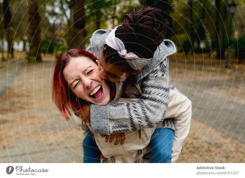 Fröhliche multirassische Freundin im Herbst im Park Huckepack Paar Huckepackverkehr umarmend Bonden Lächeln Partnerschaft Zusammensein lgbt Homosexualität