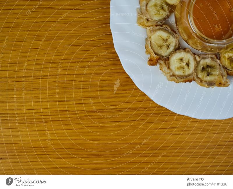 Leckere gebratene Scheiben der reifen Kochbanane und ein Glas Honig, das einen Bienenstock auf einem runden Holzteller bildet. Ansicht von oben Kochbananen
