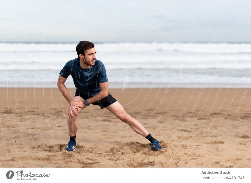 Männlicher Sportler in aktiver Kleidung bei Übungen für die Beine am leeren Strand Training Dehnung Ausfallschritt passen Lifestyle Gesundheit männlich Mann