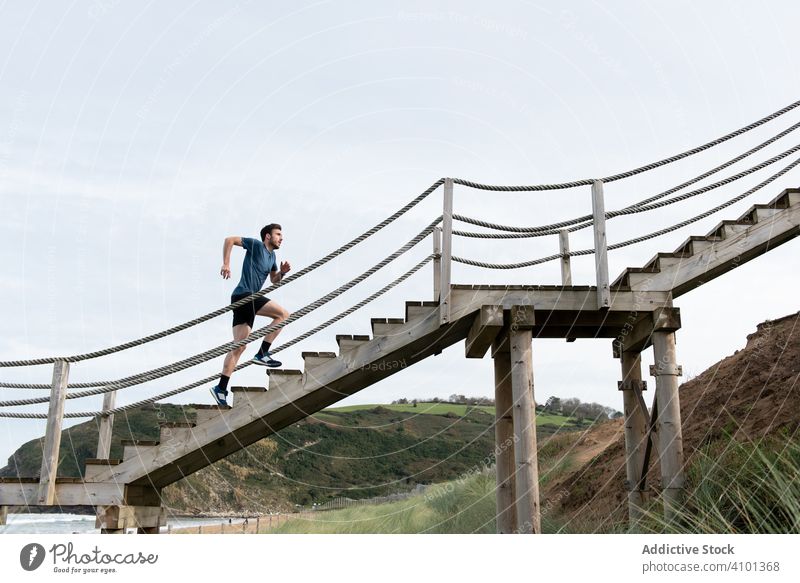 Sportler läuft auf einer Treppe am Ufer mit Bergen rennen nach oben Strand Hügelseite Himmel Zug Training Gesundheit Lifestyle passen schlank Schritt sportlich