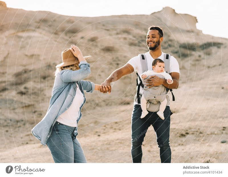 Verschiedene Eltern tanzen beim Laufen mit Baby Tanzen Familie Glück Lächeln Sand wüst Spaziergang führen Spaß Natur neugeboren heiter Lifestyle modern Kind