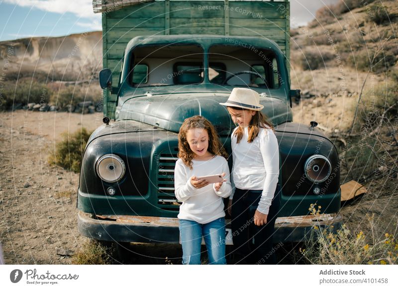 Fröhliche Mädchen beobachten Smartphone in der Nähe von verlassenen LKW Kinder Lastwagen PKW Verlassen fokussiert ruhen Lachen Lächeln heiter zuschauen